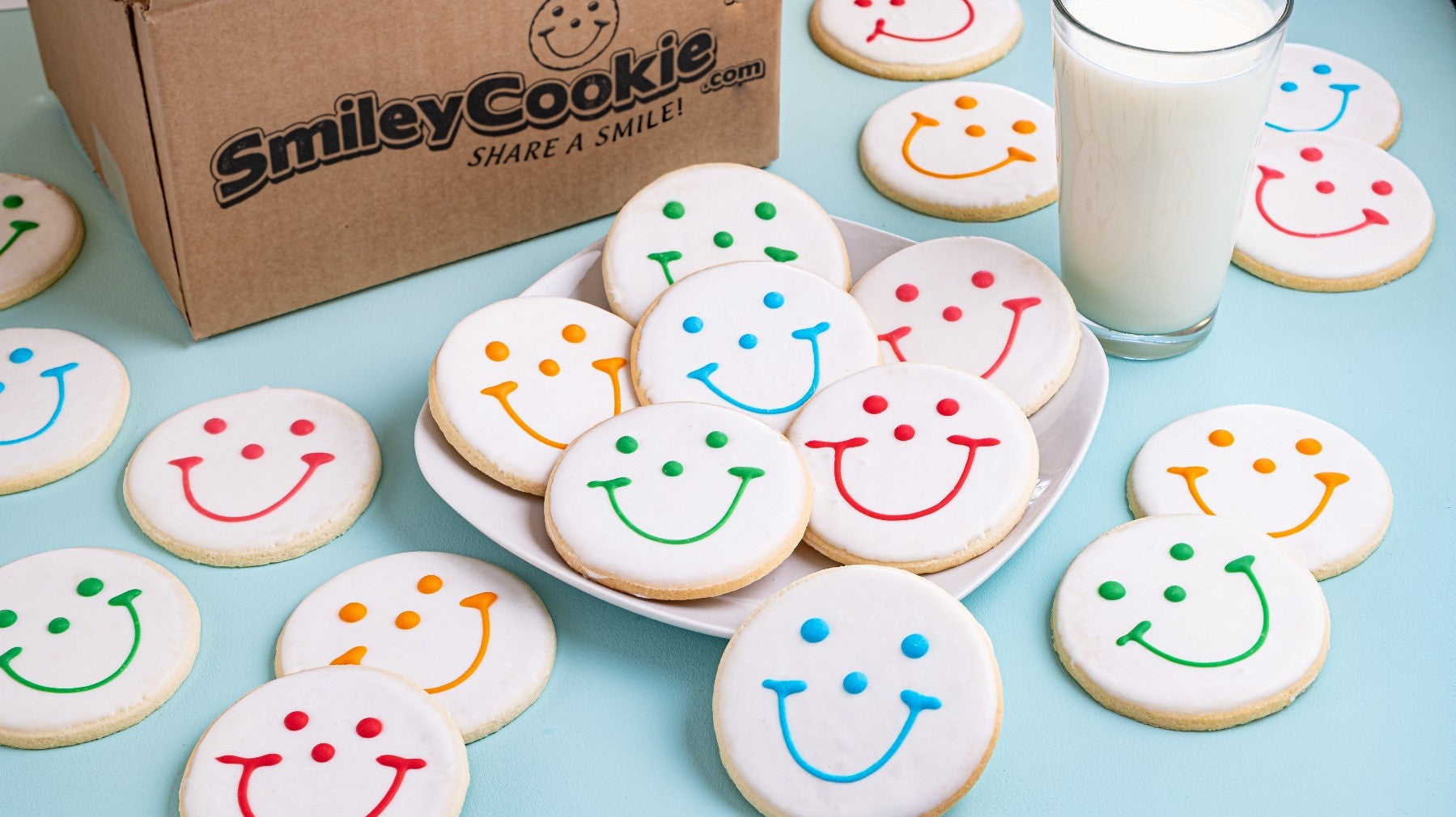 A plate of smiley face cookies with a refreshing glass of milk on a blue table cloth