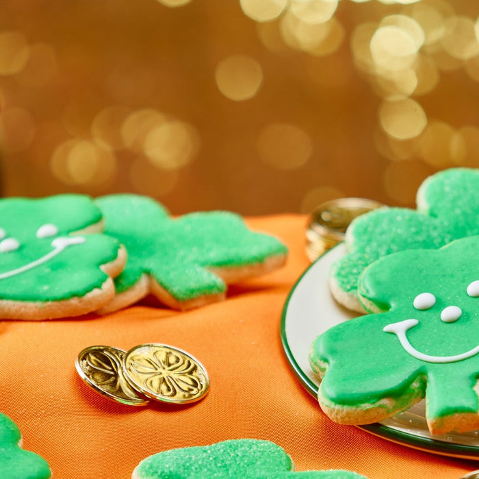 Green Shamrock cookies with smiley faces and sparkling sugar on a gold backtround with a pot of gold in the backround for St. Patrick's Day 