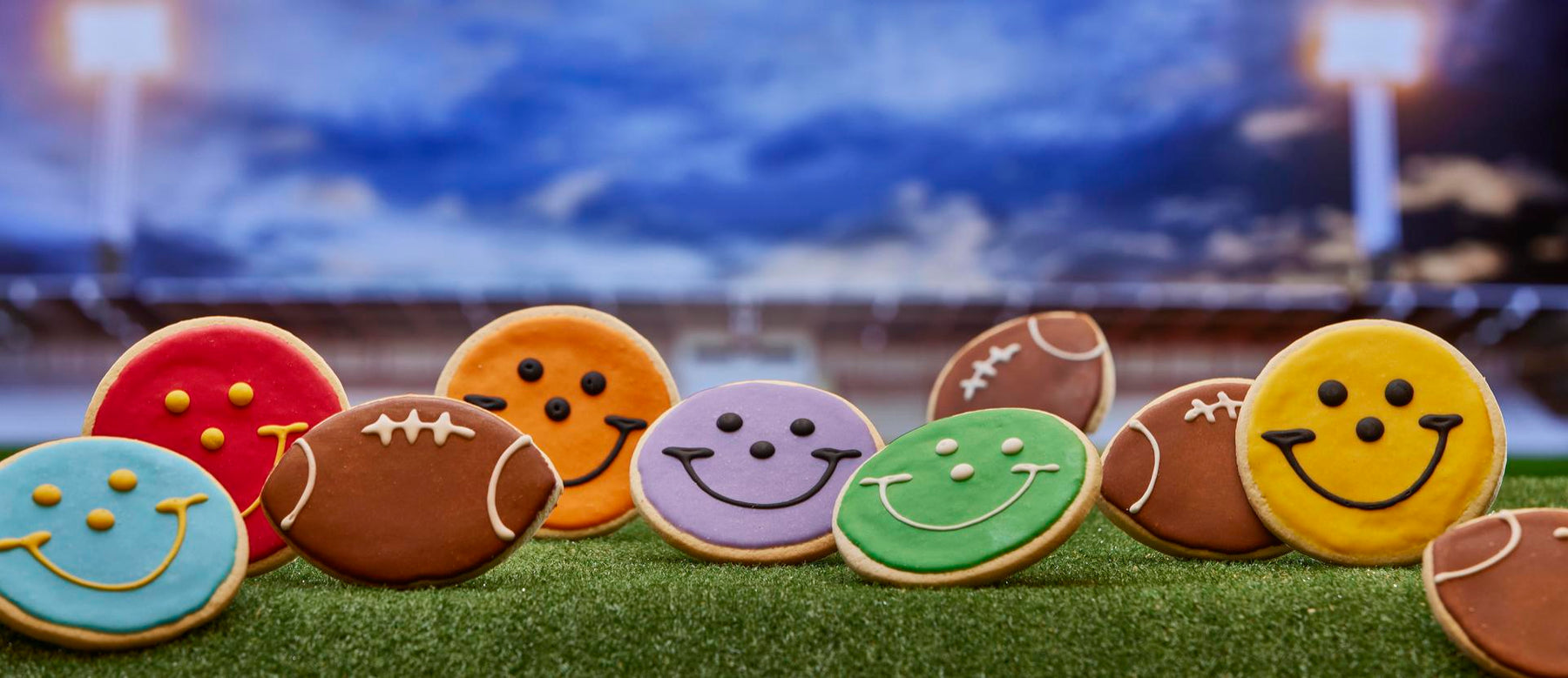 an array of smiley face cookies decorating in football team colors along with football shaped cookies on a football field backdrop